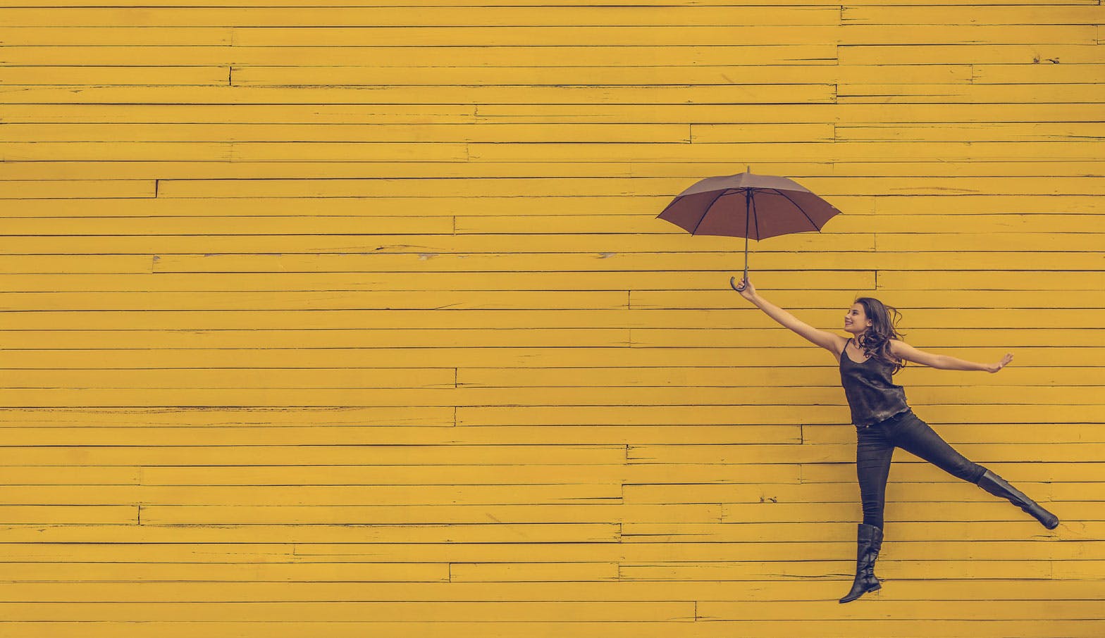 A woman with an umbrella posing in front of a yellow wall